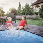 Happy cute sibling, boy and girl, have a fun and splashing each other near the swimming pool